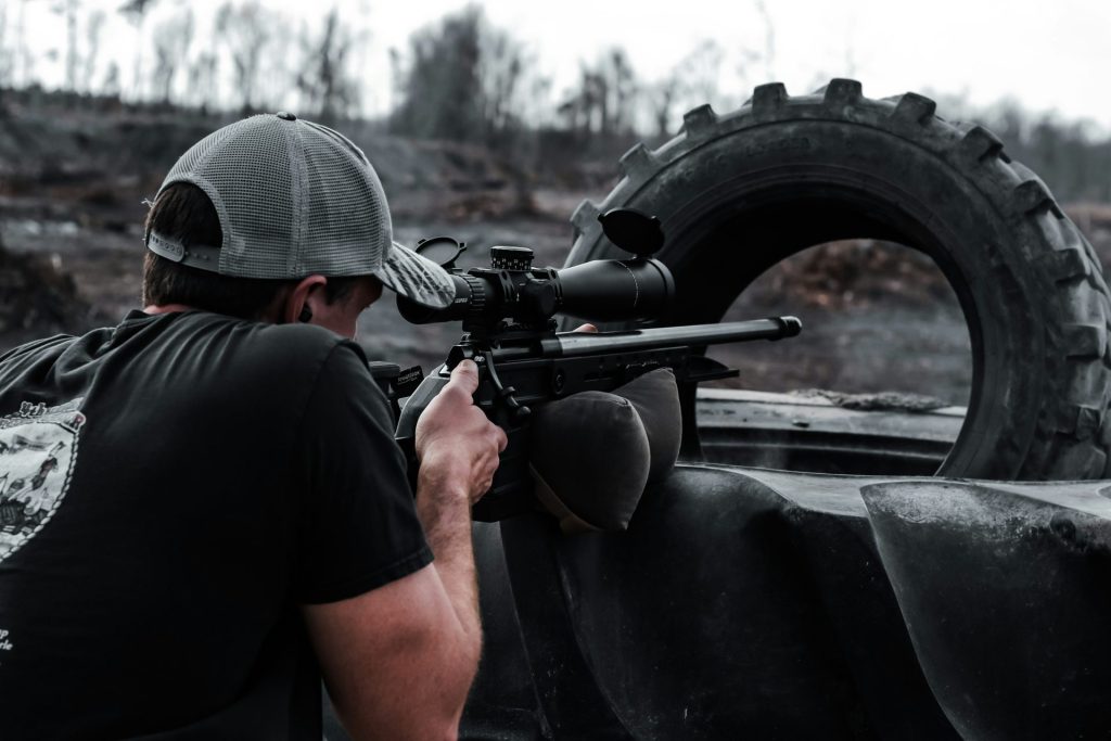 A person aims a rifle through a tire.